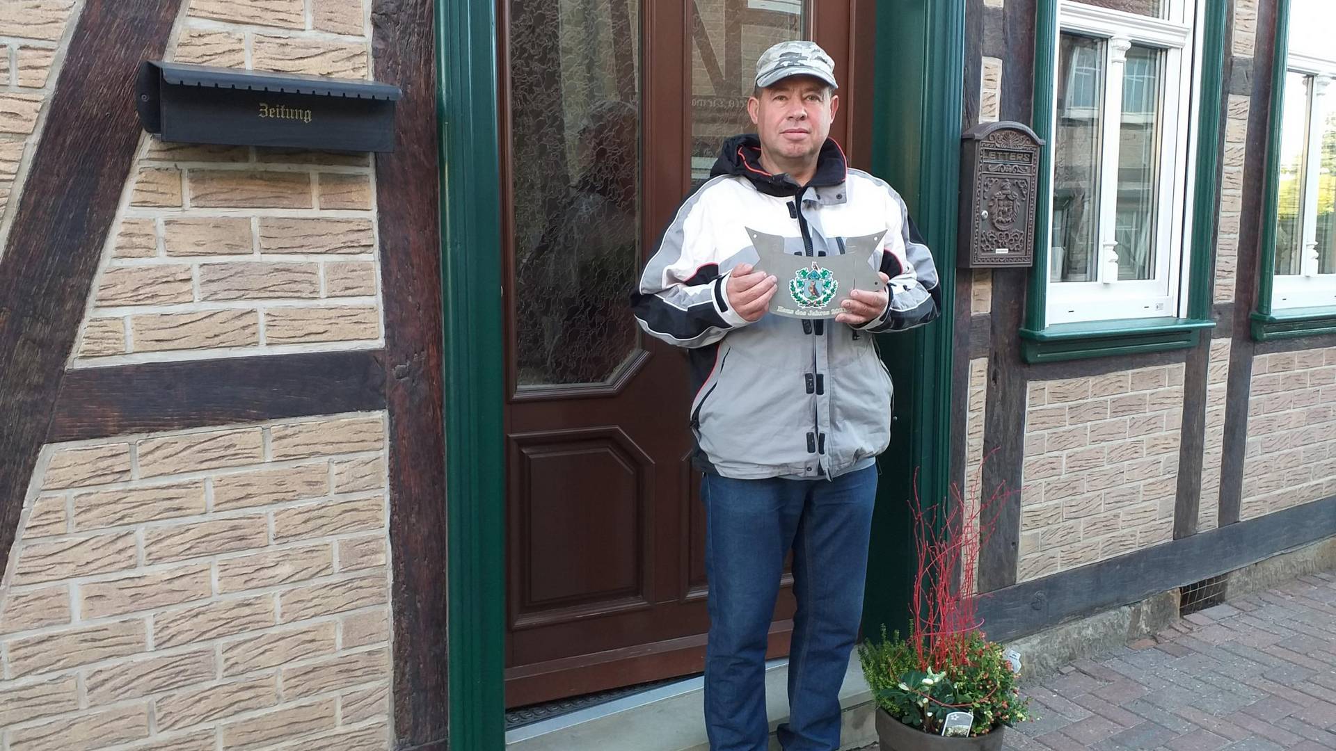 Hartmut Flohr vor seinem Haus mit Plakette und Blumenpräsent