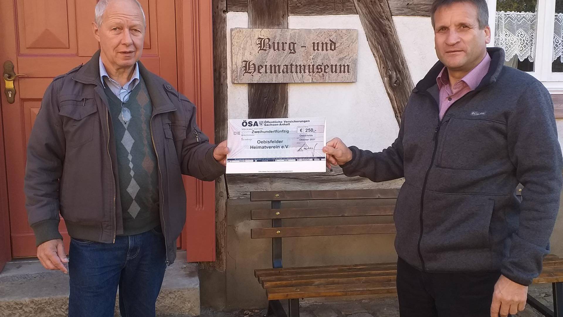 Roy Langhof über gibt vor dem Burg- und Heimatmuseum Ulrich Pettke den Scheck