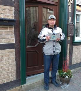 Hartmut Flohr vor seinem Haus mit Plakette und Blumenpräsent