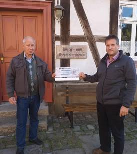 Roy Langhof über gibt vor dem Burg- und Heimatmuseum Ulrich Pettke den Scheck